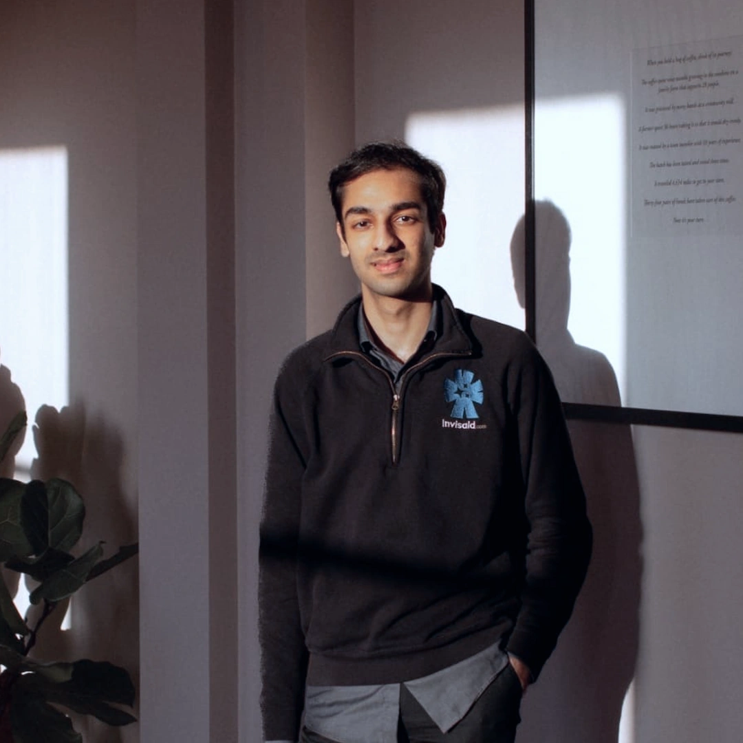 A portrait of Abdul, the founder and director of Invisaid. He is standing in an office with a black quarter-zip on.